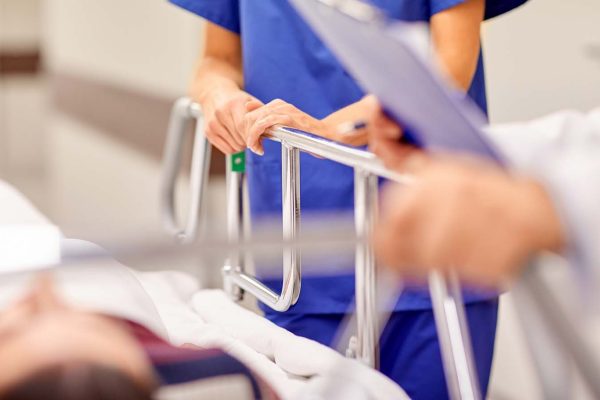Pflegekraft hilft einem Patienten im Krankenbett mit einem Rollbrett.